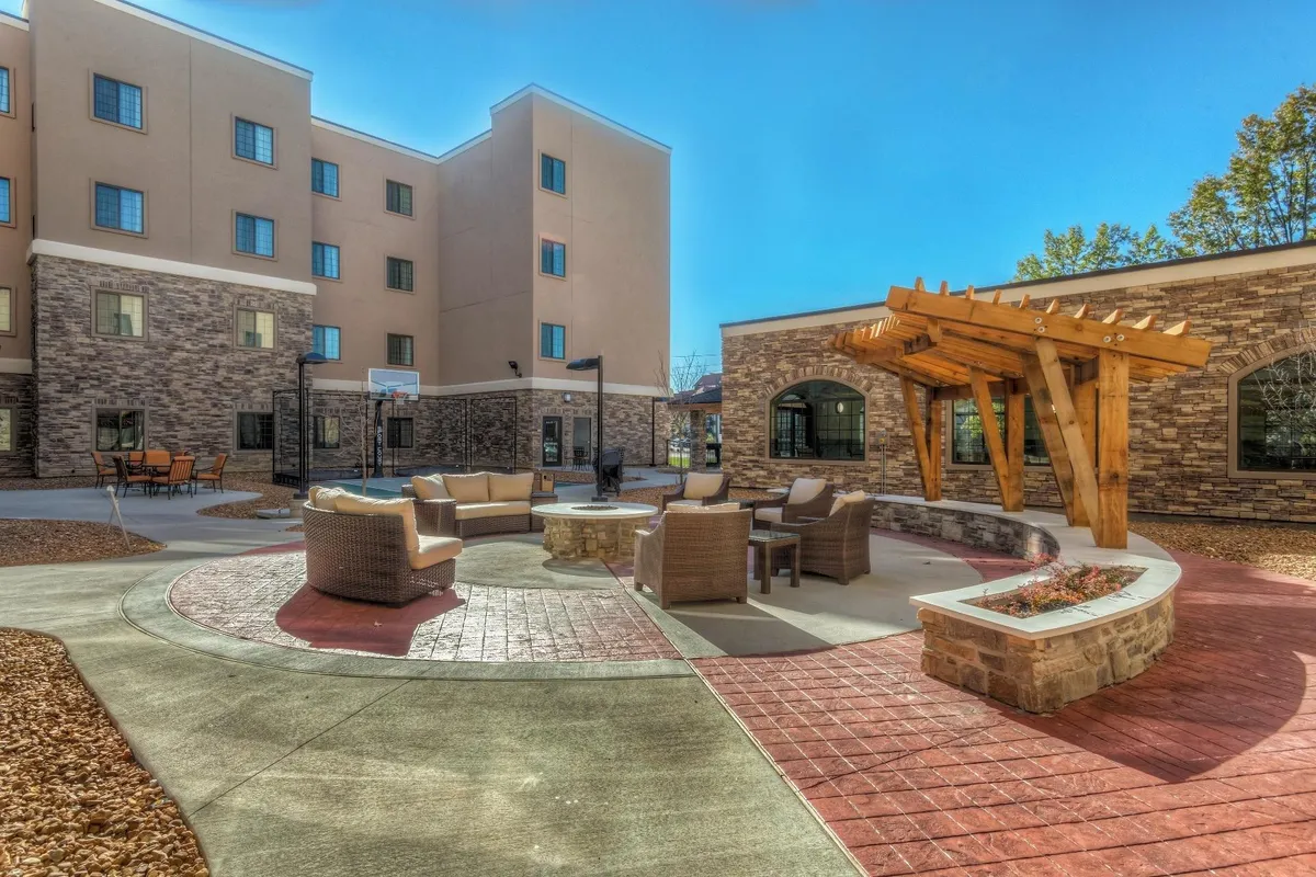 This exterior scene shows a spacious seating area under a wooden pergola, with a stone fire pit and plenty of tables and chairs for social gatherings and outdoor meals.