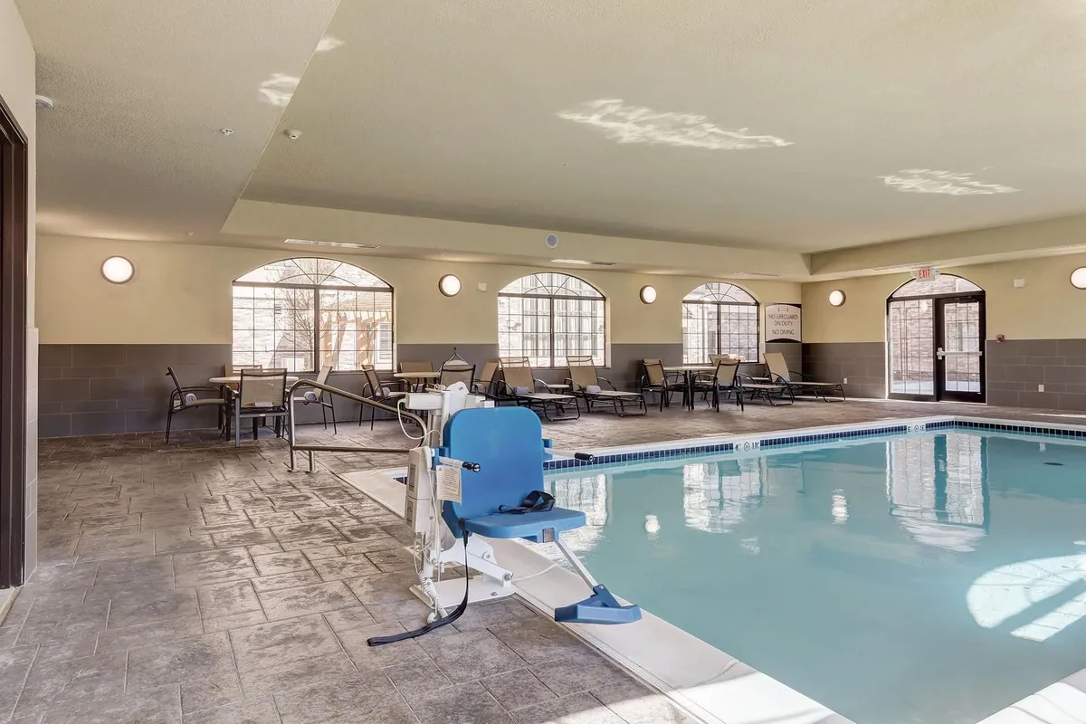 A serene indoor swimming pool area with poolside seating and an accessible lift. The space feels welcoming, inviting relaxation, socializing, and even light exercise like swimming or yoga.