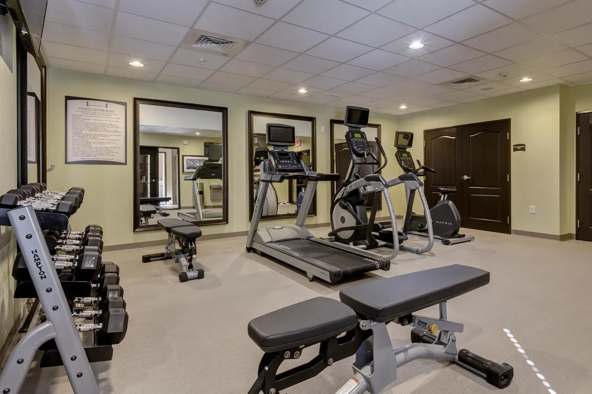 A well-equipped fitness center featuring a treadmill, elliptical machine, free weights, and mirrors, all set in a motivating and clean environment. The space is designed for solo or group workouts, encouraging productivity and well-being for busy travelers.