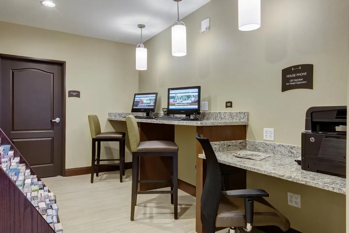 A business center with computers, bar stools, and a granite countertop provides a productive environment for checking emails or planning itineraries. The modern setup is both practical and comfortable, mirroring the multifunctional aspect of the kitchen and dining area.