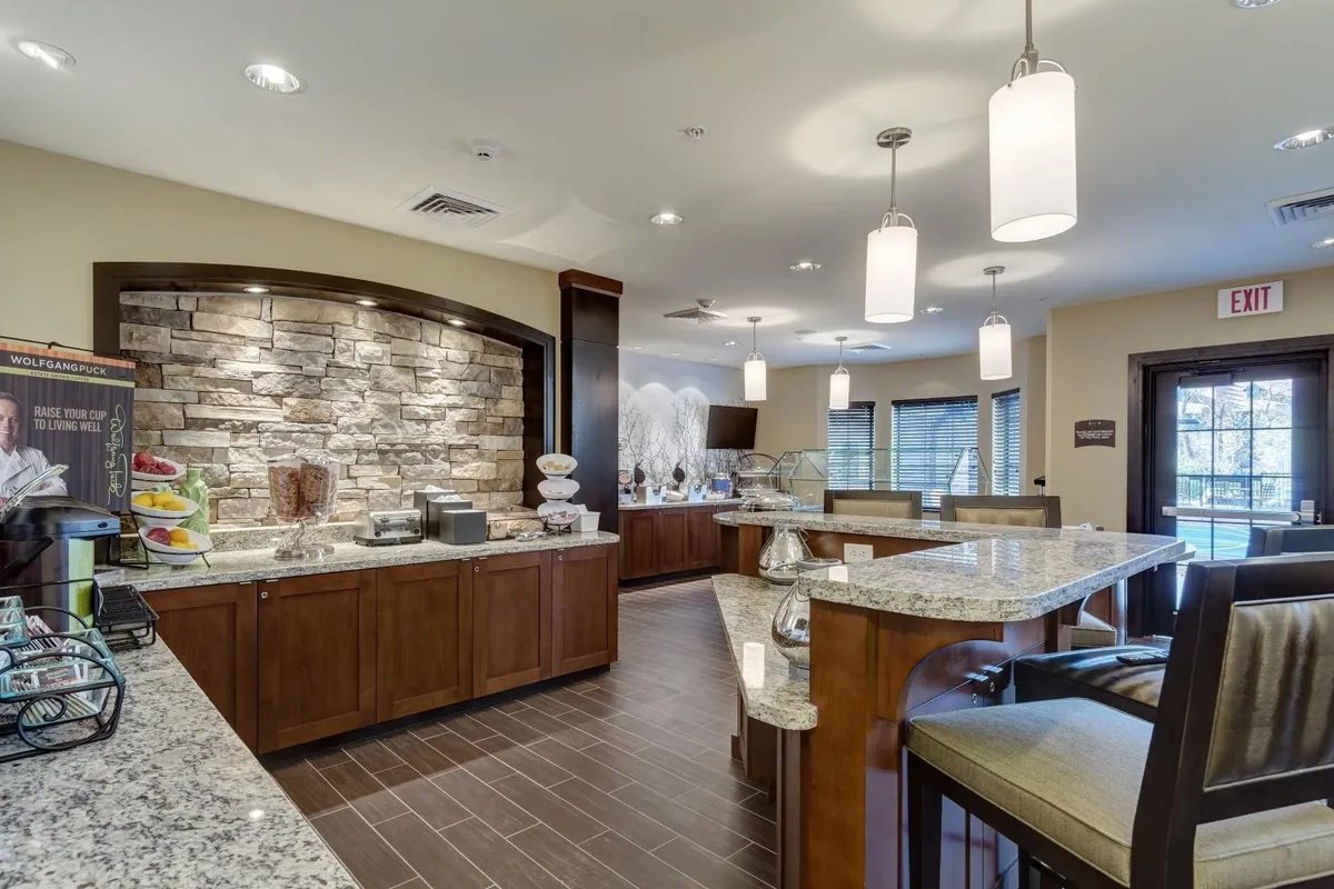 This image shows a cozy interior space featuring a granite countertop, a stone feature wall, stylish lighting fixtures, and a seating area. The setting captures the feel of a welcoming communal hub where guests can enjoy breakfast, sip coffee, or gather for casual chats.
