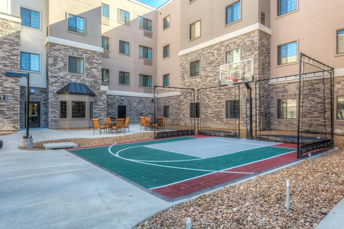 The image captures the exterior of the property, featuring a lively basketball court, comfortable outdoor seating, and the building’s façade. It hints at the energetic and social environment families can enjoy outdoors together.