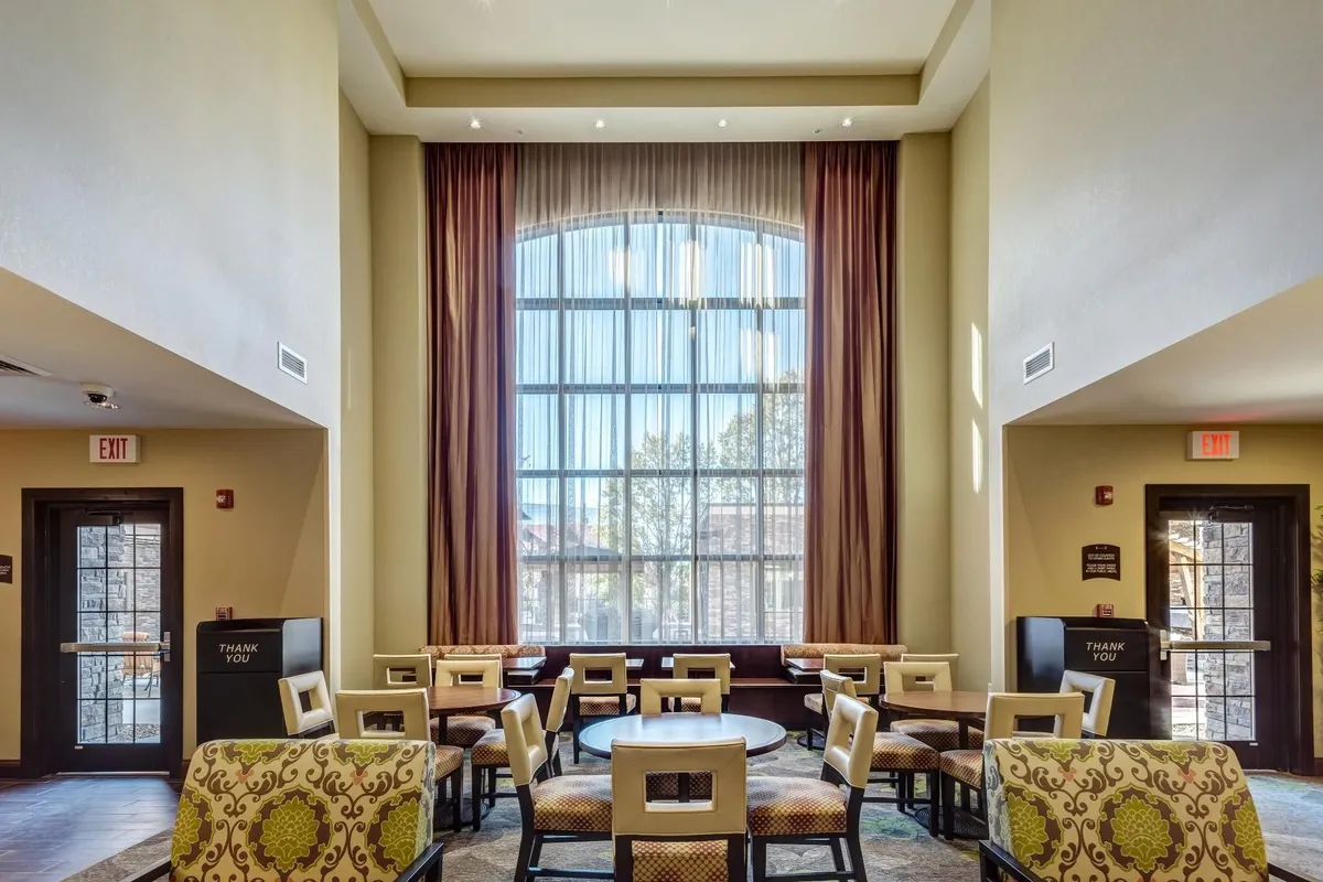 A cozy and bright interior seating area with a large arched window, decorative chairs, and wooden doors. Sunlight fills the space, creating a warm, inviting atmosphere ideal for relaxing or socializing.