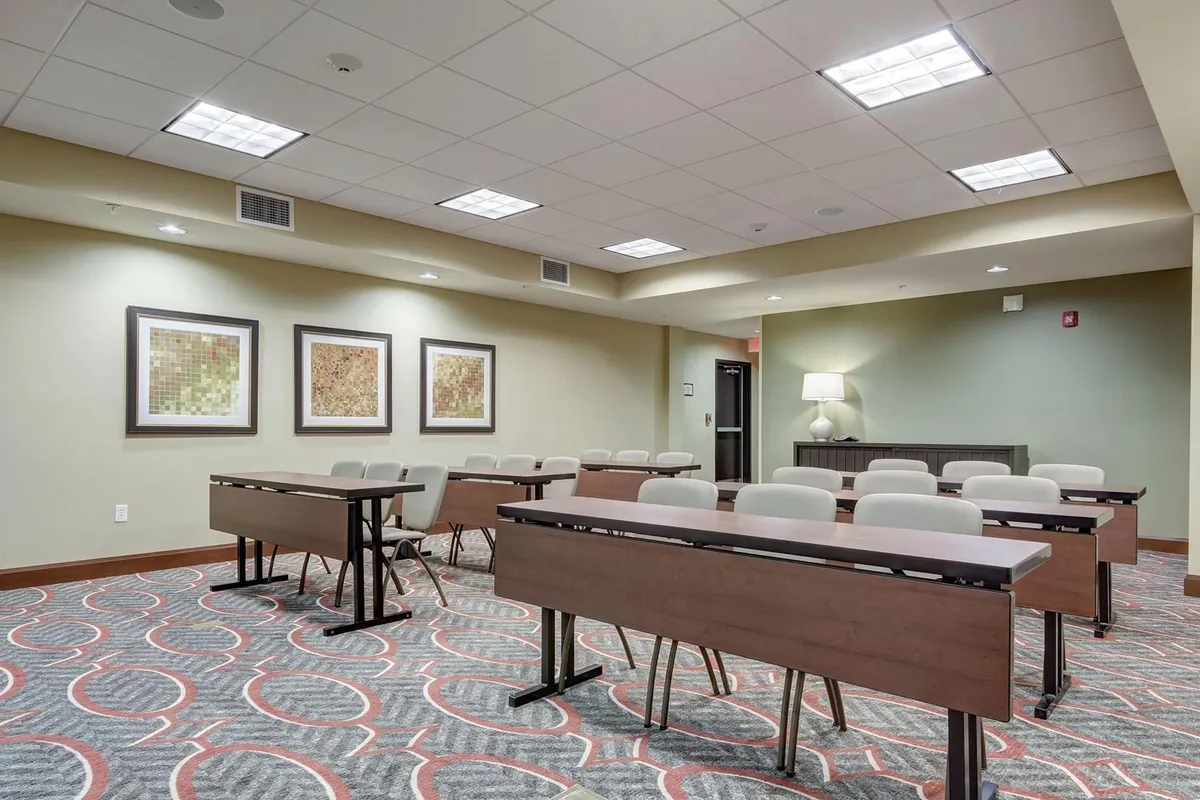 A modern business center with wooden conference tables, comfortable chairs, and framed artwork on the walls. The setup is clean and professional, offering a well-lit space for meetings, workshops, and remote work.
