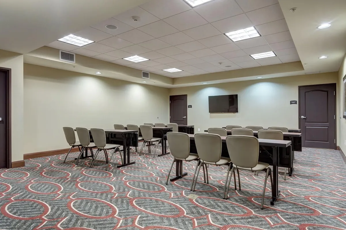 A well-appointed meeting or lounge space with tables, chairs, and a wall-mounted TV, designed for collaborative activities or quiet work. The mood is focused yet welcoming, supporting both productivity and social interaction.