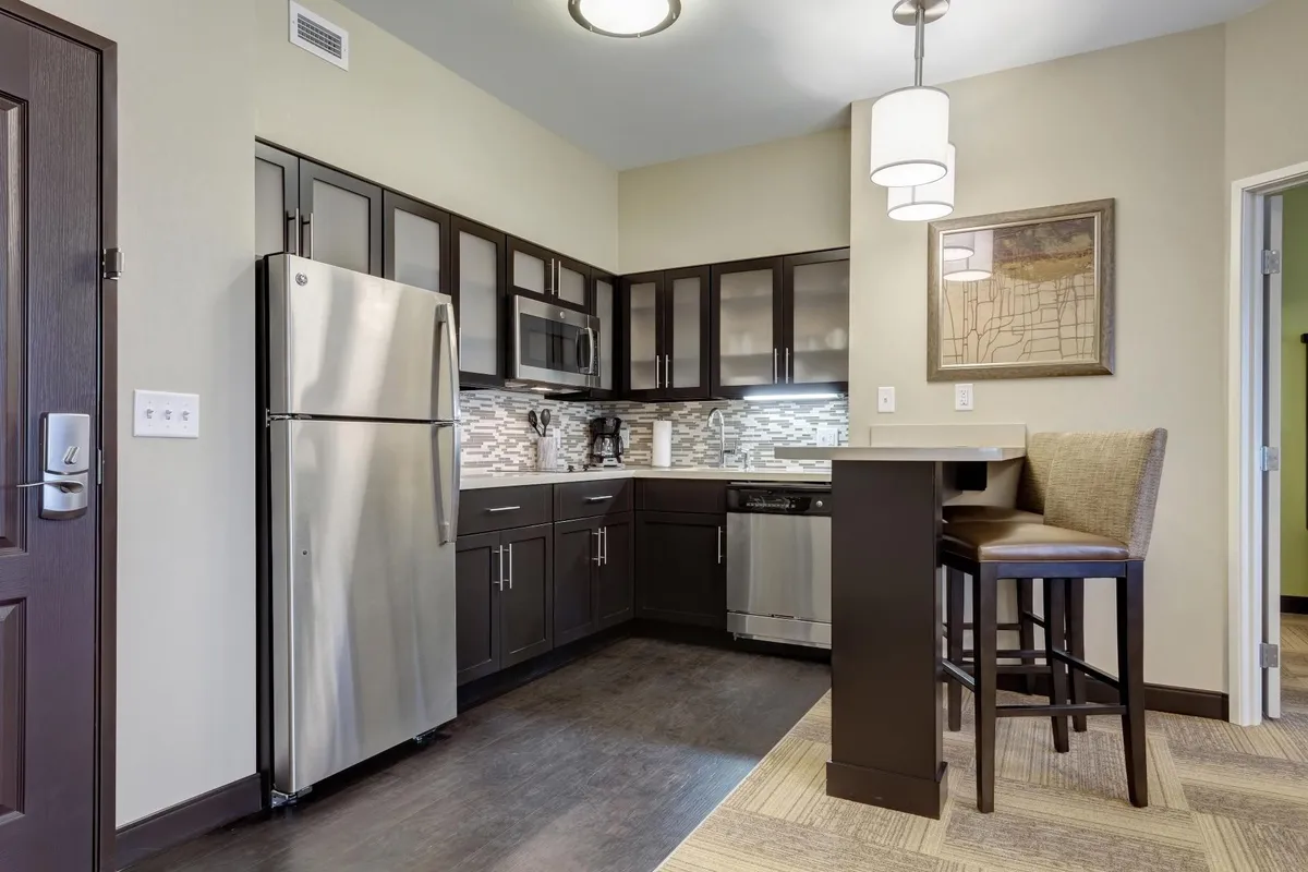 A stylish kitchen and dining area, featuring a stainless steel refrigerator, contemporary dark cabinetry, modern bar stools, and decorative wall art. The space is arranged for casual dining and social gatherings, inviting shared laughter and home-cooked meals.
