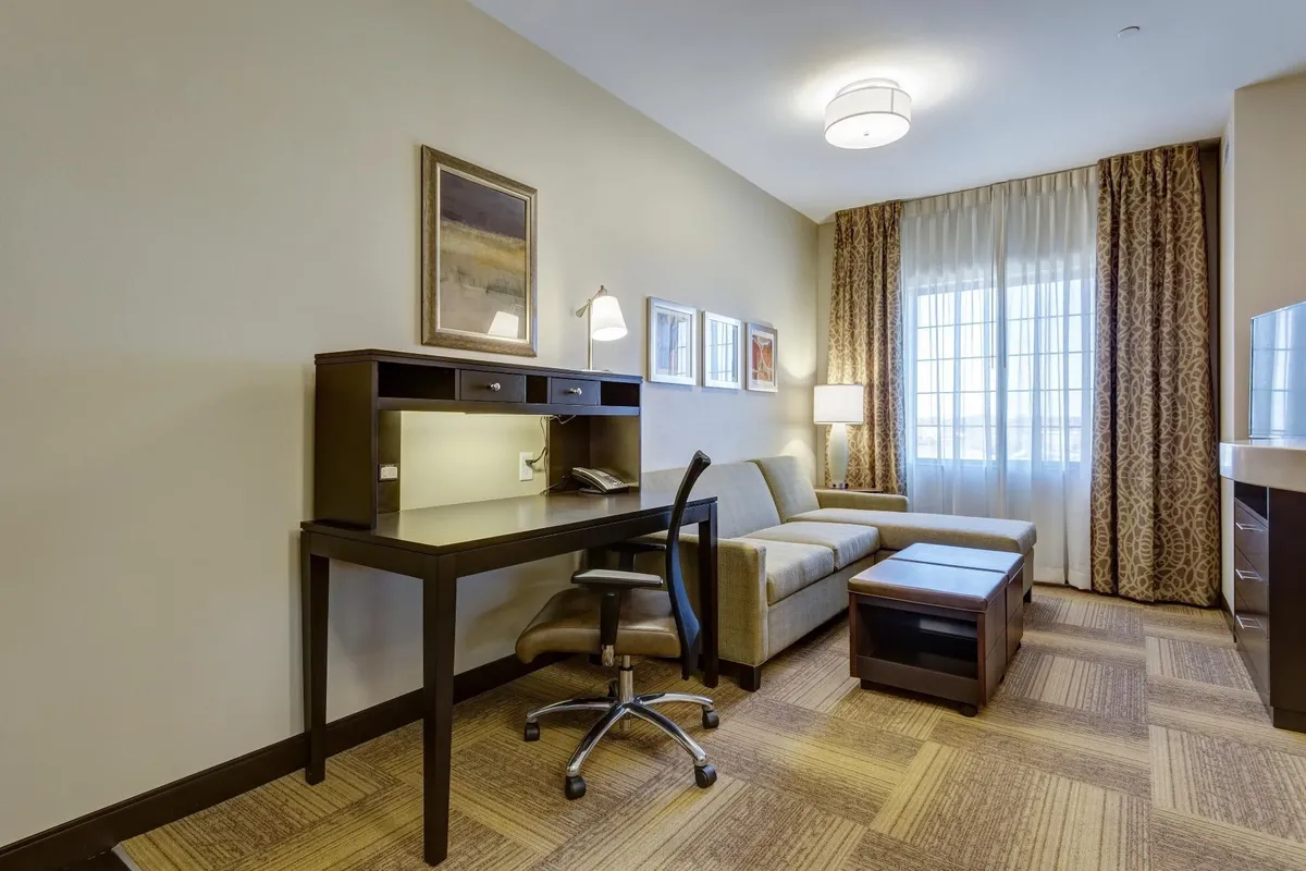 The image showcases a cozy condo interior featuring a comfortable sofa, a well-lit work desk by the window, a glowing table lamp, and tasteful wall art, creating a welcoming and multi-functional living space.