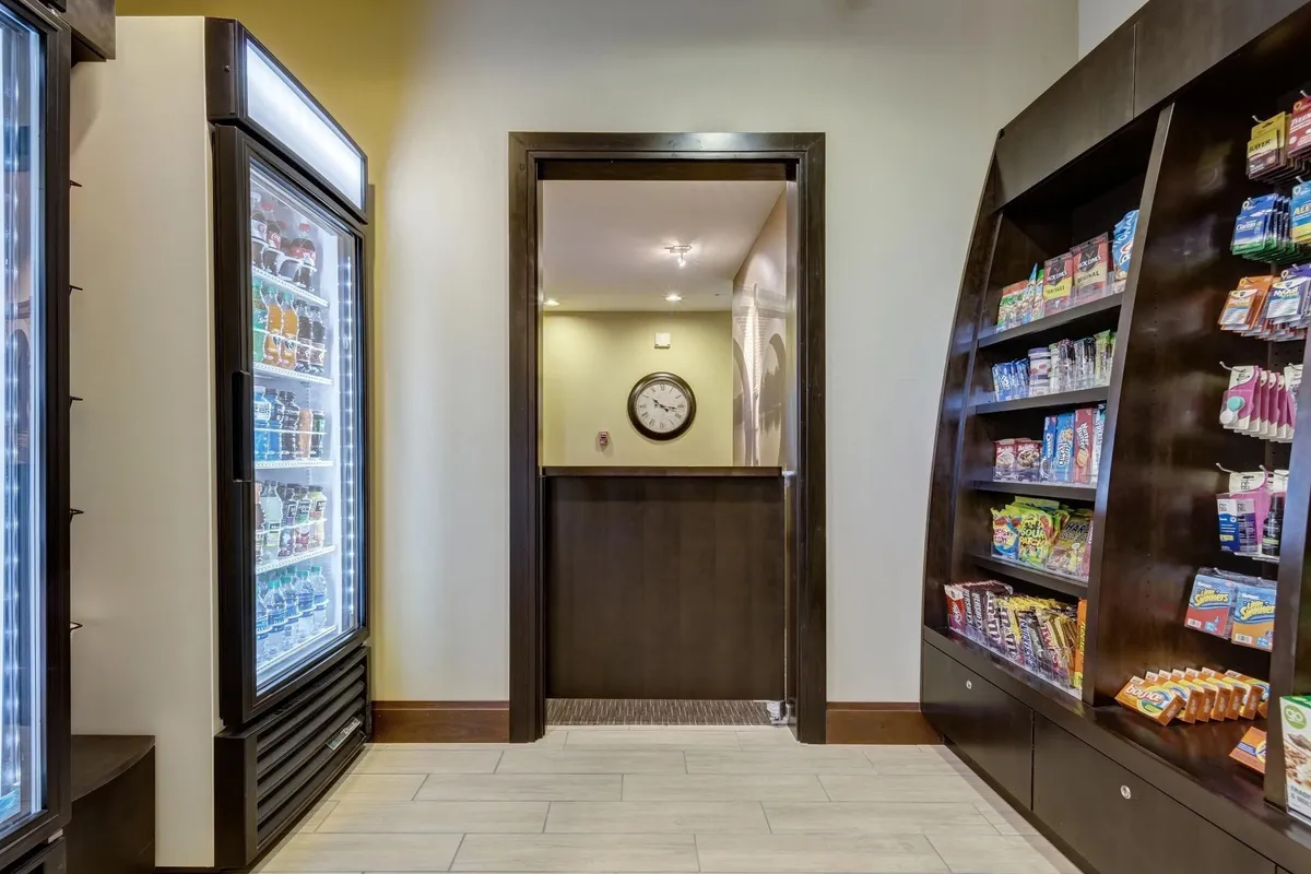 A convenient snack and drink area with a refrigerated display, snack shelves, and a wall clock, creating a casual spot for quick refreshments or social interaction between meetings.