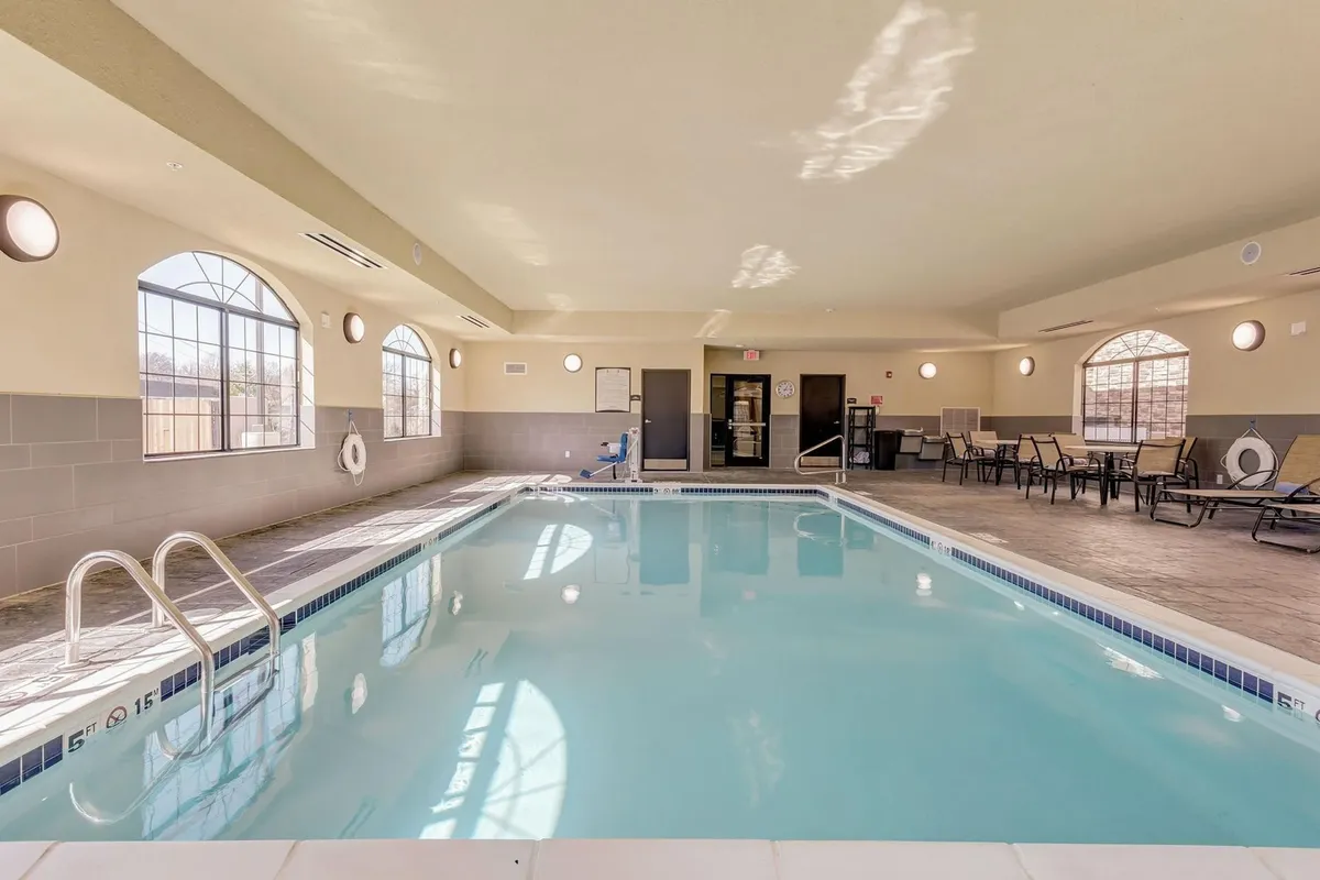 A bright and inviting indoor pool area with large windows allowing natural light to pour in, comfortable lounge chairs poolside, and clean poolside tiles. The tranquil environment is ideal for unwinding after a day of meetings or taking a rejuvenating swim in the evening.