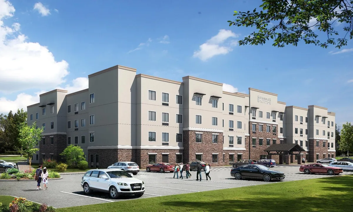 The image showcases the exterior of the building, emphasizing the entrance canopy, landscaped grounds, and conveniently located parking area. The mood is inviting and friendly, signaling a warm welcome and easy access for guests arriving by car.